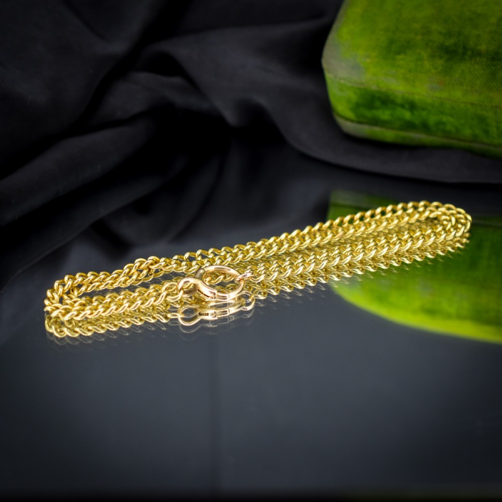 An antique 18ct yellow gold curb link chain necklace featuring a circular bolt ring clasp on a green velvet surface. View V