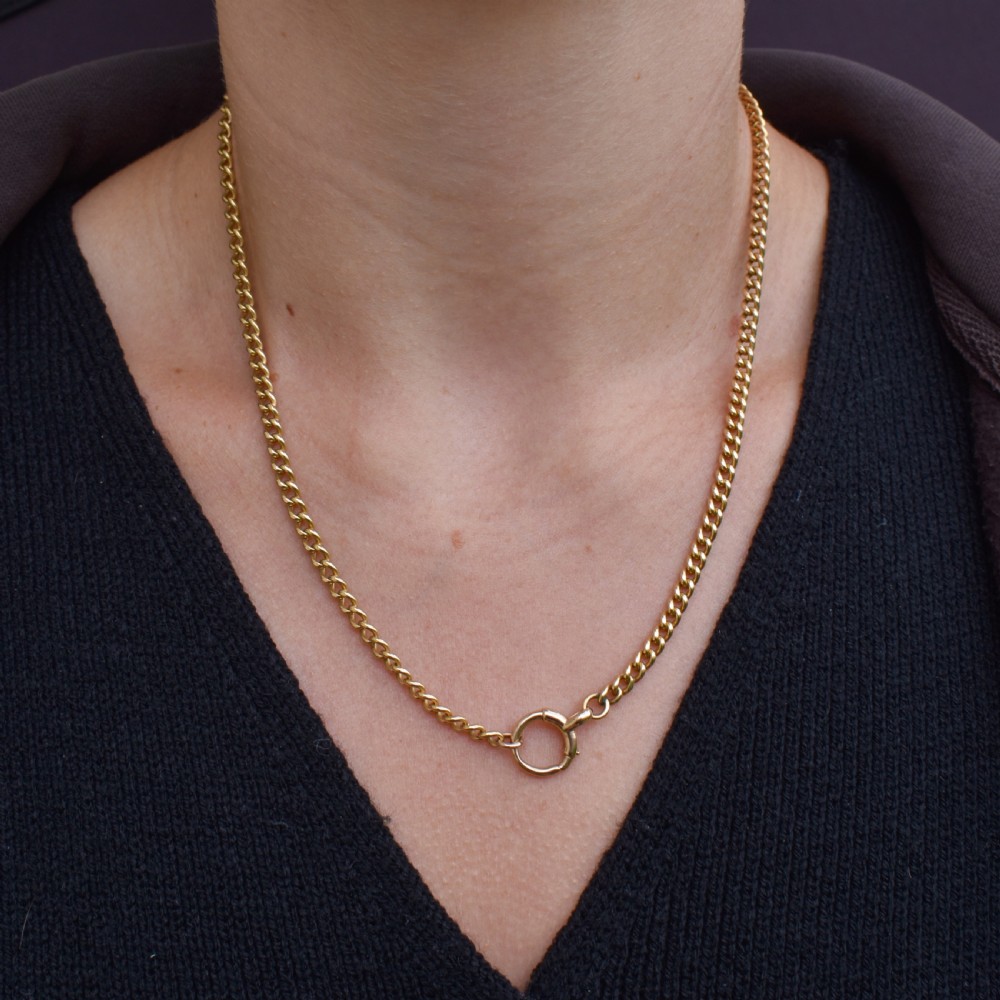 An antique 18ct yellow gold curb link chain necklace featuring a circular bolt ring clasp on a green velvet surface. View IX