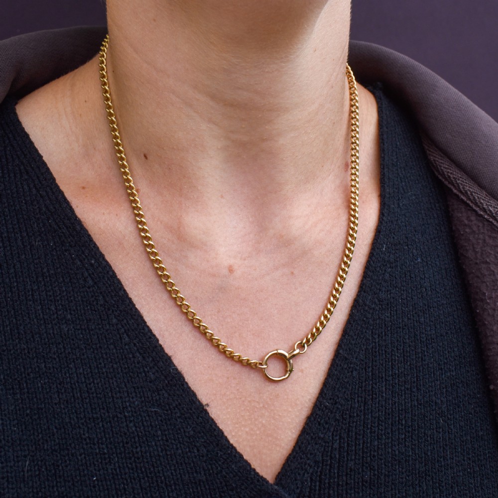 An antique 18ct yellow gold curb link chain necklace featuring a circular bolt ring clasp on a green velvet surface. View X