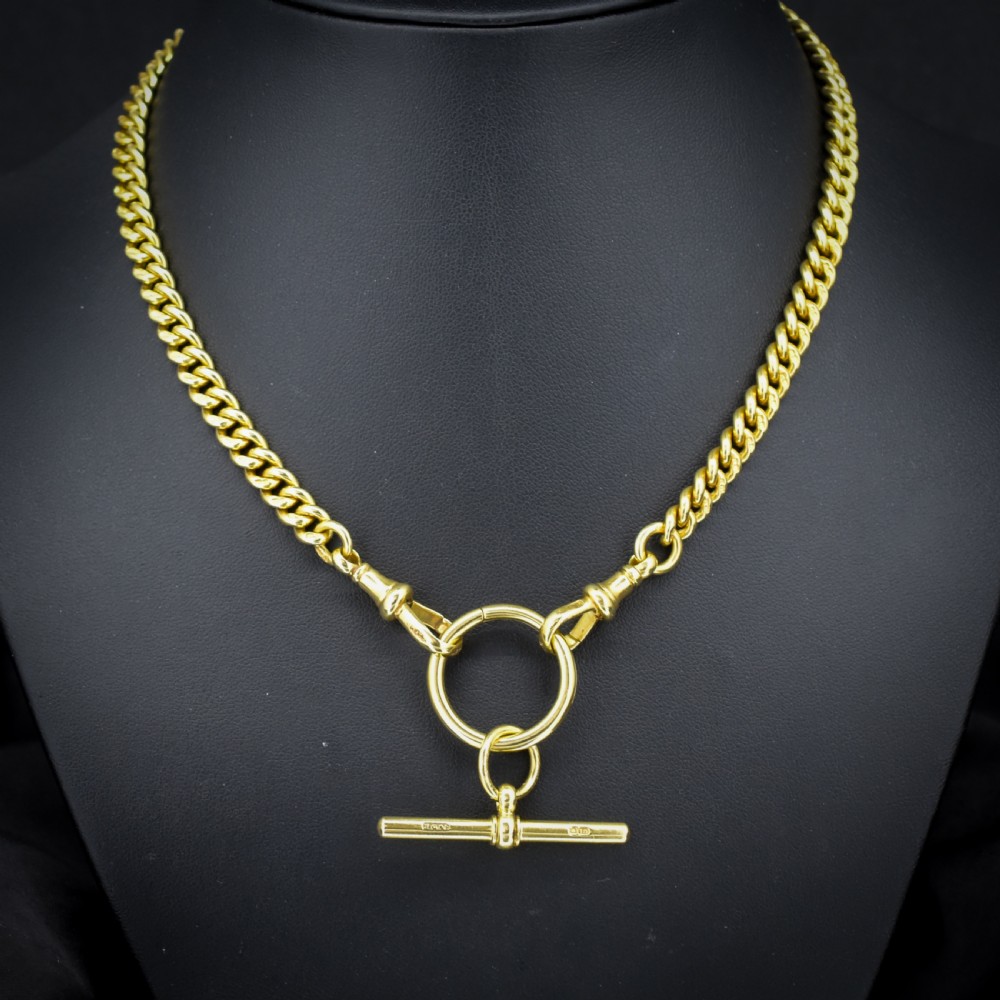 An 18ct yellow gold curb link Albert chain necklace featuring a central ring with a T-bar drop, displayed on a black jewellery bust.