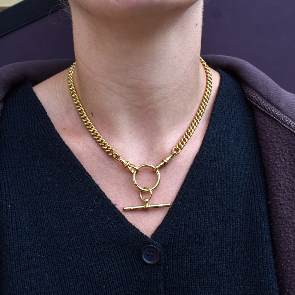 An 18ct yellow gold curb link Albert chain necklace featuring a central ring with a T-bar drop, displayed on a black jewellery bust. View X
