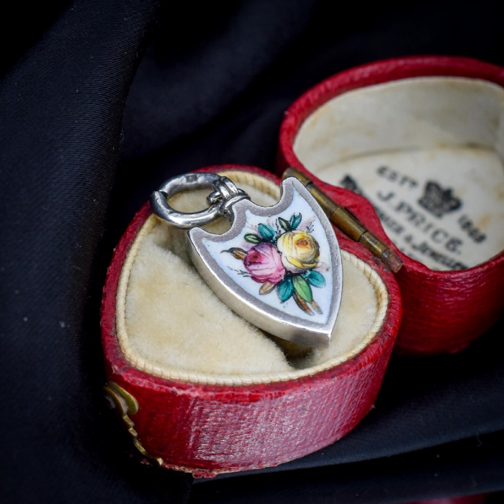 An antique shield-shaped silver pendant featuring hand-painted pink and yellow roses on a white enamel background.