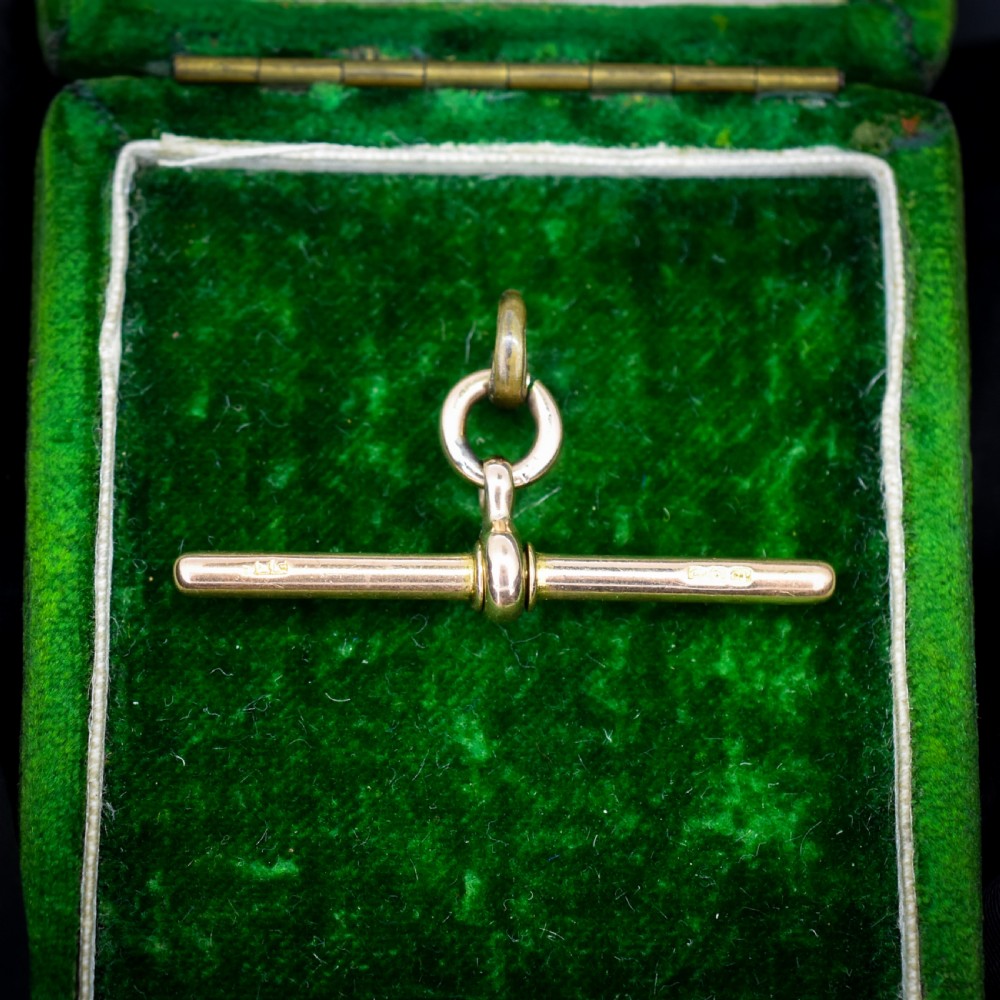 An antique 15ct yellow gold T-bar pendant featuring a smooth crossbar, central jump rings, and stamped British hallmarks.