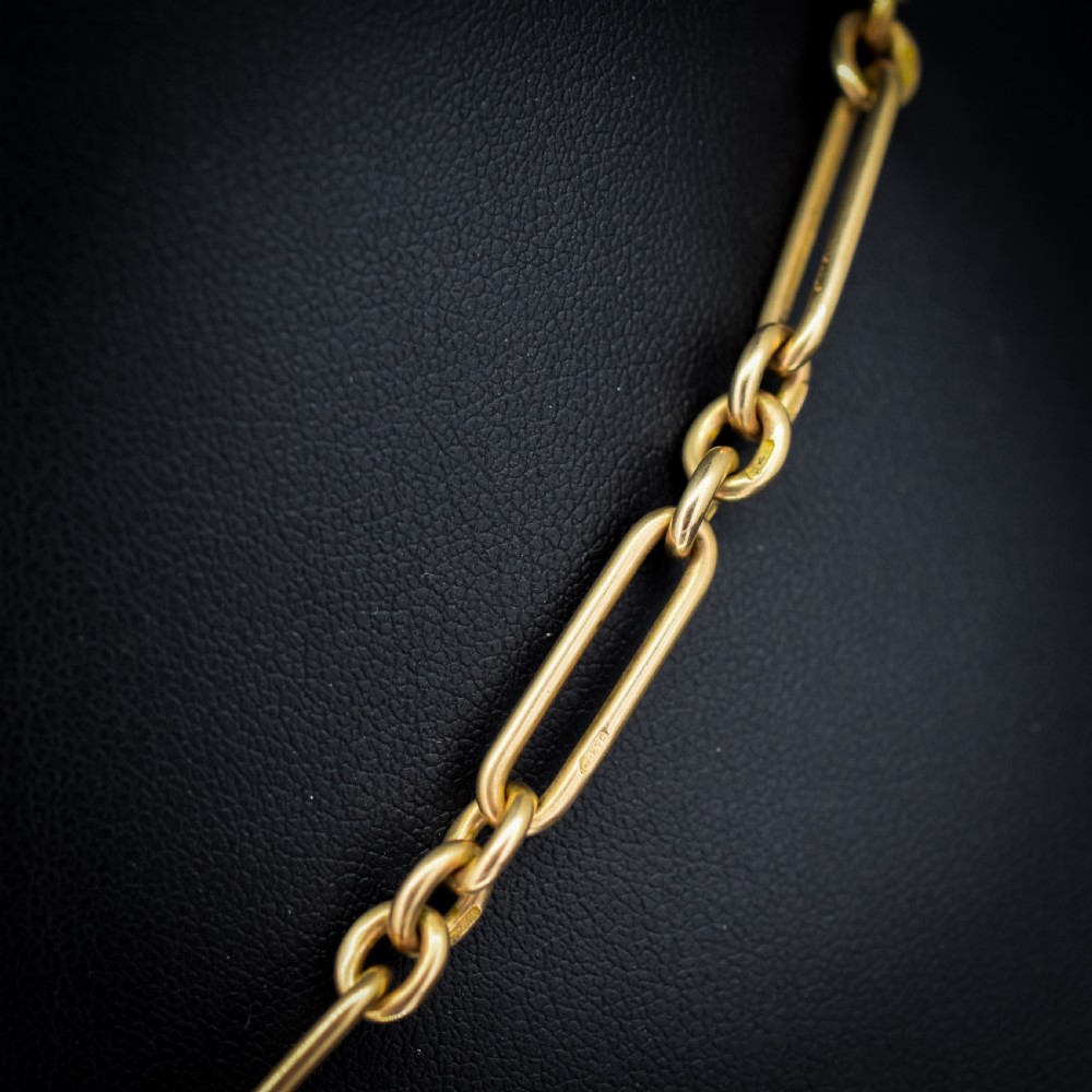 A 9ct yellow gold Art Deco Albert watch chain featuring alternating elongated trombone links, a swivel clasp, and a T-bar. View V