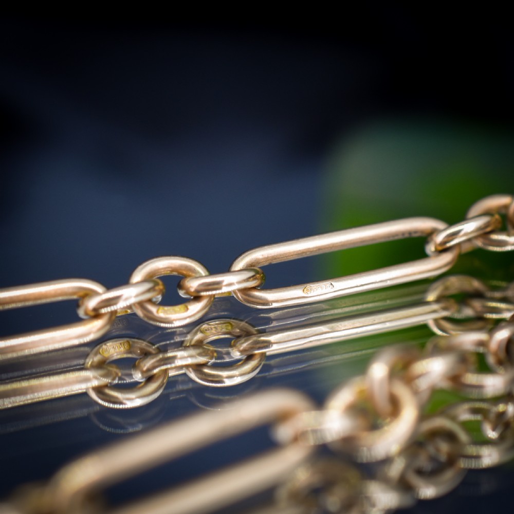 A 9ct yellow gold Art Deco Albert watch chain featuring alternating elongated trombone links, a swivel clasp, and a T-bar. View X