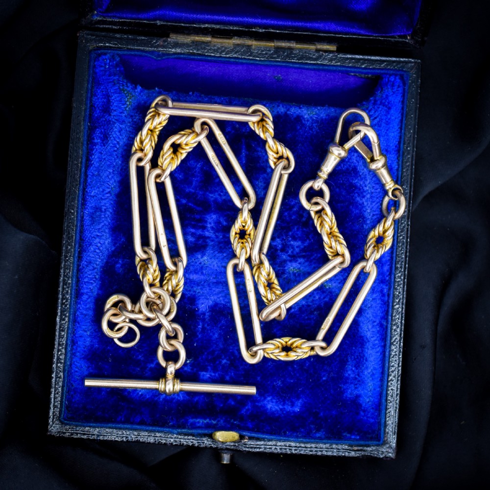 A 9ct yellow gold Albert chain featuring alternating elongated trombone links and textured love knot links with a T-bar and swivel clasp.