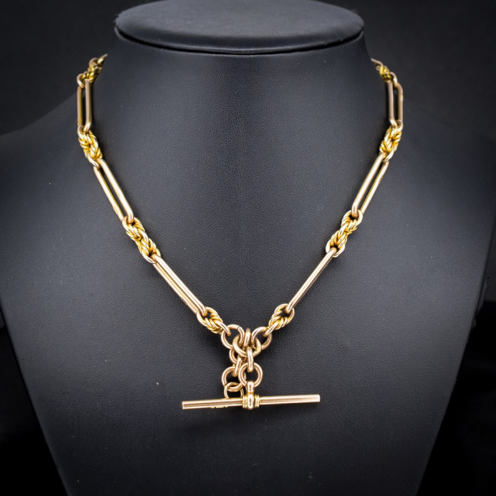 A 9ct yellow gold Albert chain featuring alternating elongated trombone links and textured love knot links with a T-bar and swivel clasp. View II