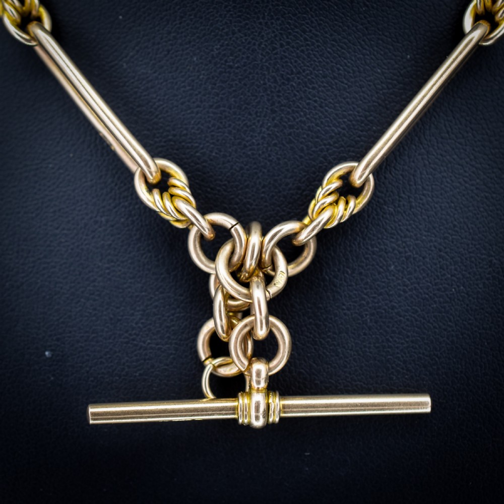 A 9ct yellow gold Albert chain featuring alternating elongated trombone links and textured love knot links with a T-bar and swivel clasp. View III