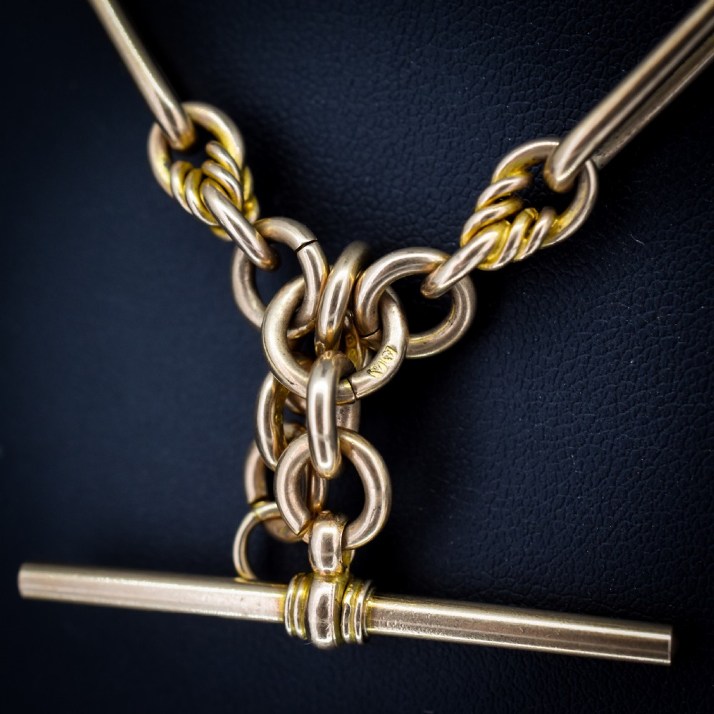 A 9ct yellow gold Albert chain featuring alternating elongated trombone links and textured love knot links with a T-bar and swivel clasp. View IV