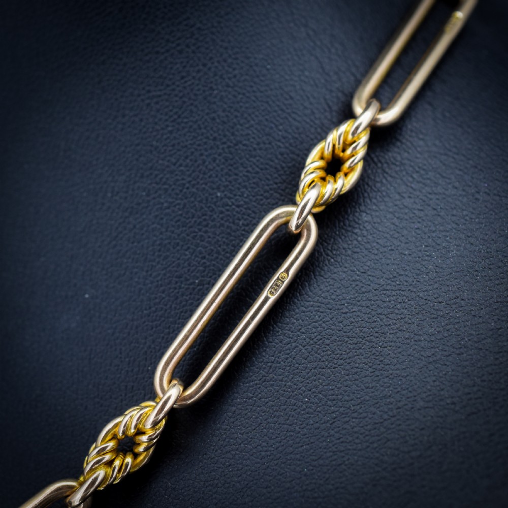 A 9ct yellow gold Albert chain featuring alternating elongated trombone links and textured love knot links with a T-bar and swivel clasp. View V