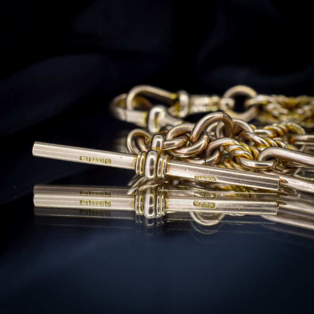 A 9ct yellow gold Albert chain featuring alternating elongated trombone links and textured love knot links with a T-bar and swivel clasp. View VII