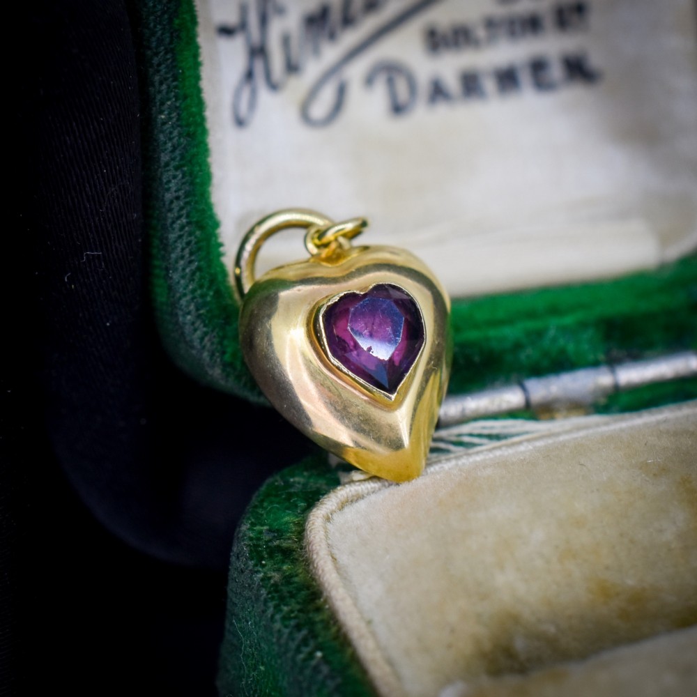 An antique yellow gold puffy heart-shaped charm featuring a central heart-cut purple amethyst paste gem.