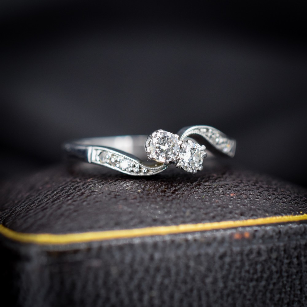 An antique 18ct white gold Toi et Moi ring featuring two central round diamonds set in a diagonal twist arrangement with diamond-set shoulders.