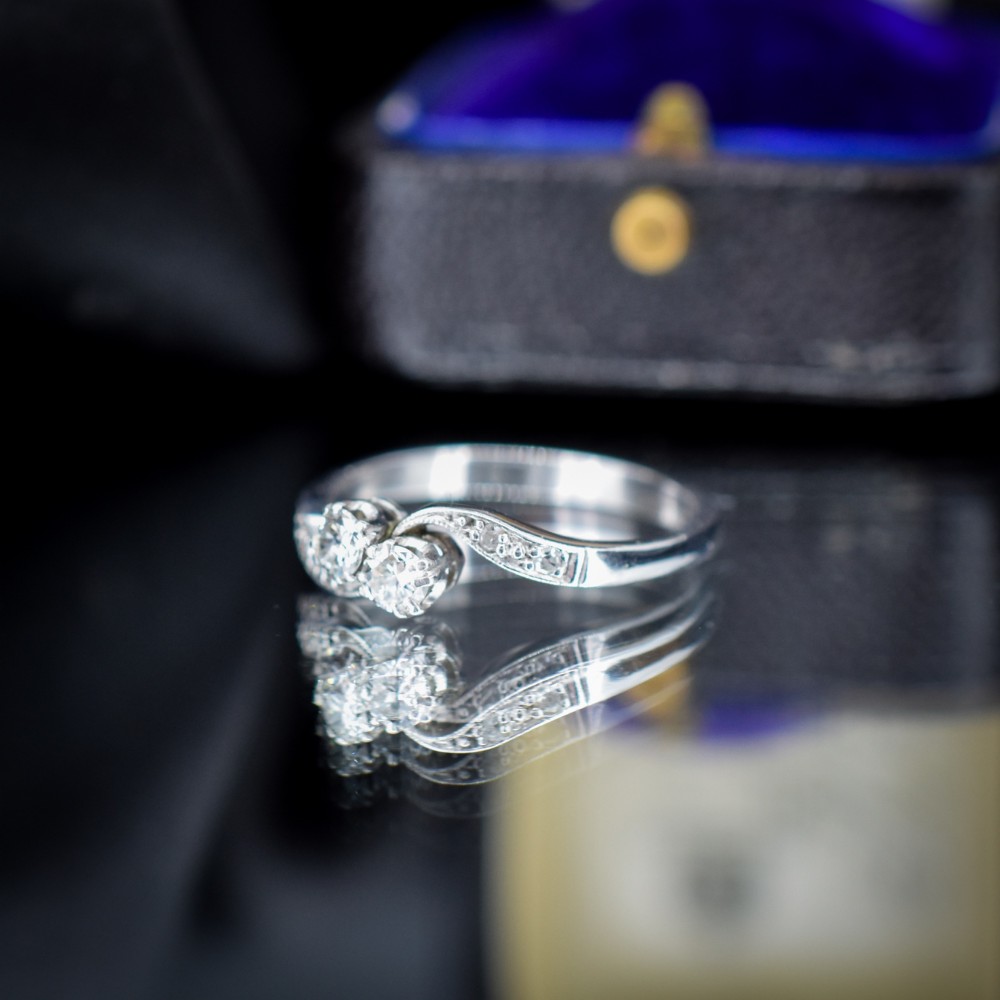 An antique 18ct white gold Toi et Moi ring featuring two central round diamonds set in a diagonal twist arrangement with diamond-set shoulders. View VI