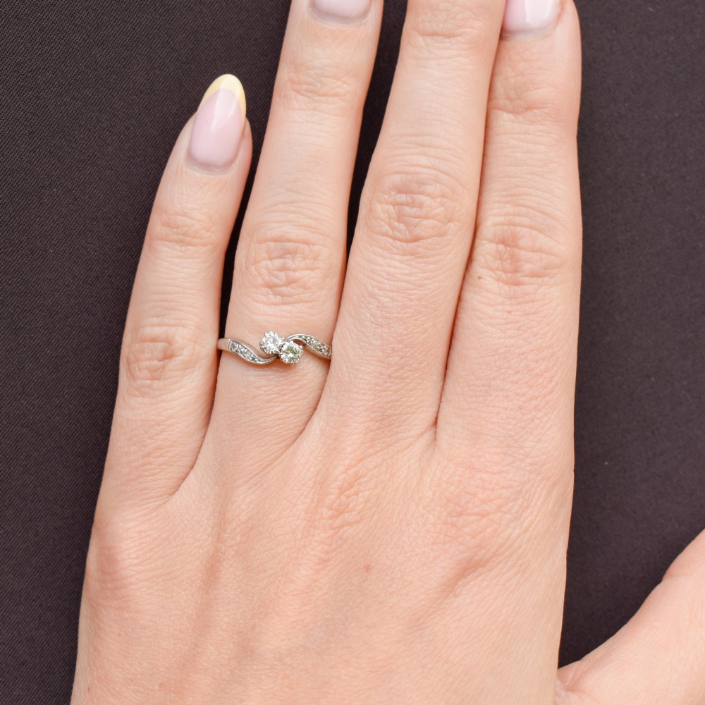 An antique 18ct white gold Toi et Moi ring featuring two central round diamonds set in a diagonal twist arrangement with diamond-set shoulders. View IX