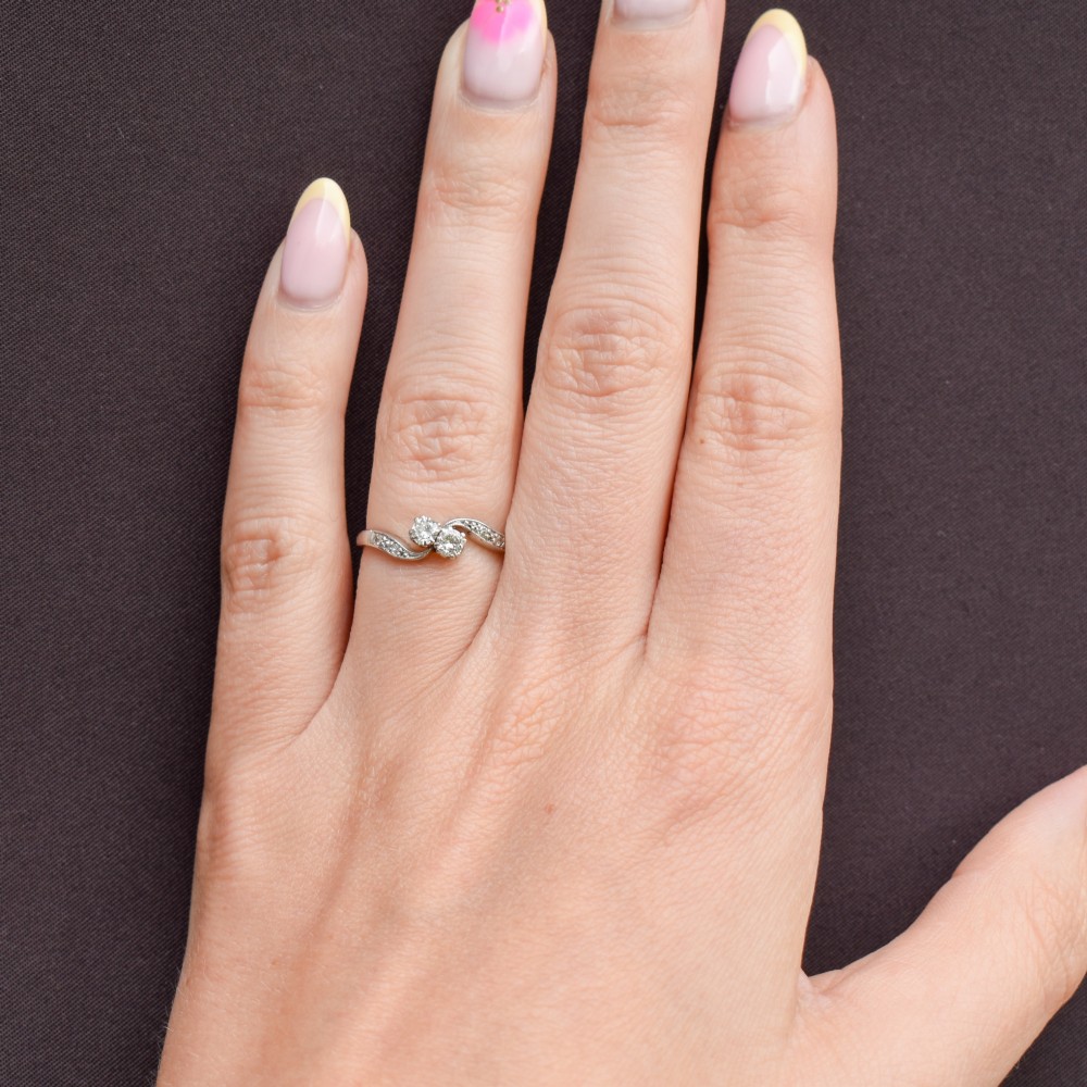 An antique 18ct white gold Toi et Moi ring featuring two central round diamonds set in a diagonal twist arrangement with diamond-set shoulders. View X