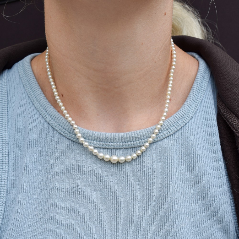 A 16-inch single strand necklace of graduated cream pearls fitted with a gold clasp. View VII