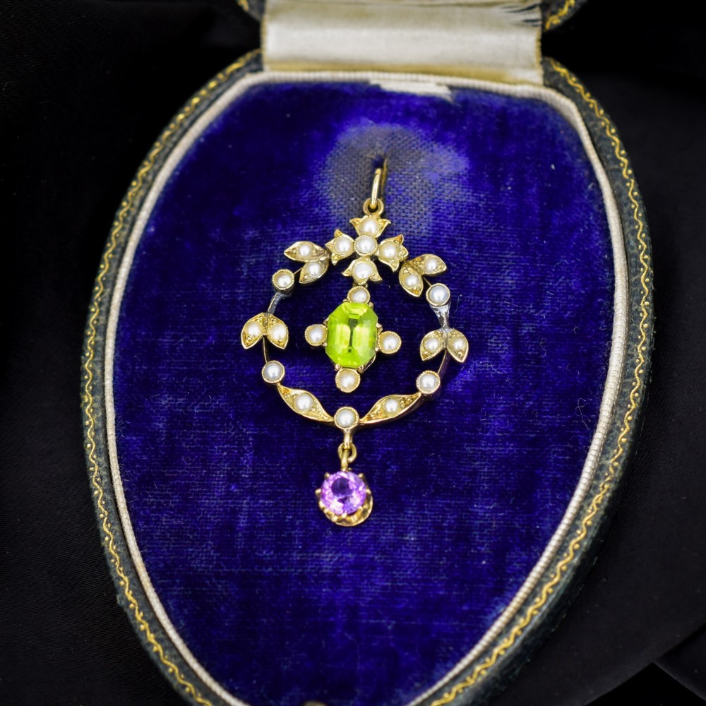 An Edwardian 15ct gold openwork lavalier pendant set with seed pearls, featuring an oval green peridot central stone and a suspended round purple amethyst drop.