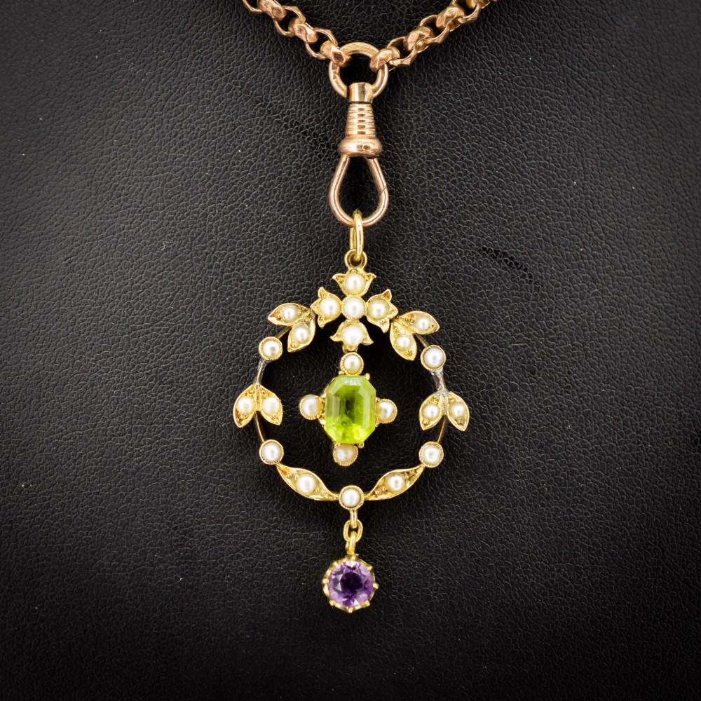 An Edwardian 15ct gold openwork lavalier pendant set with seed pearls, featuring an oval green peridot central stone and a suspended round purple amethyst drop. View IV