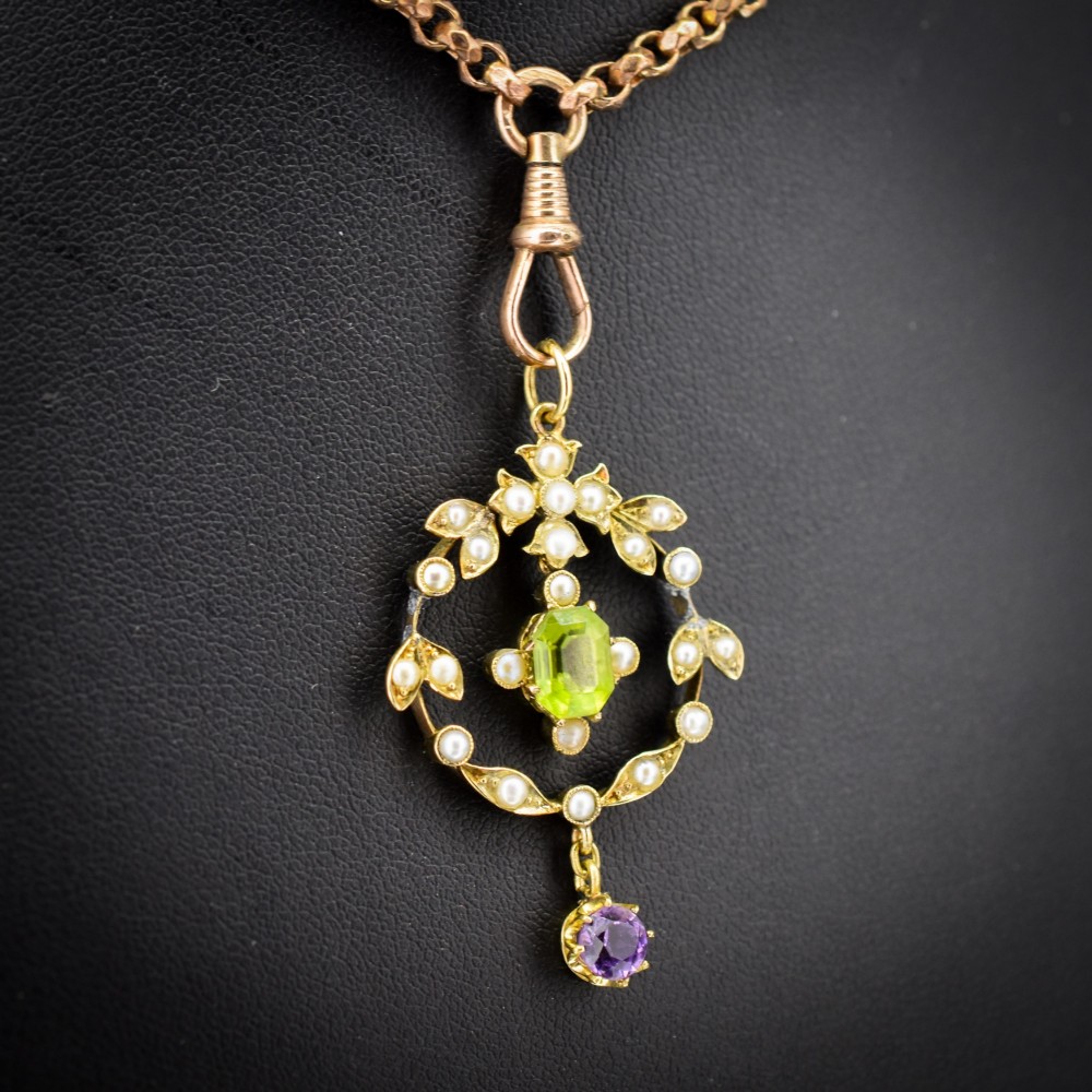 An Edwardian 15ct gold openwork lavalier pendant set with seed pearls, featuring an oval green peridot central stone and a suspended round purple amethyst drop. View V