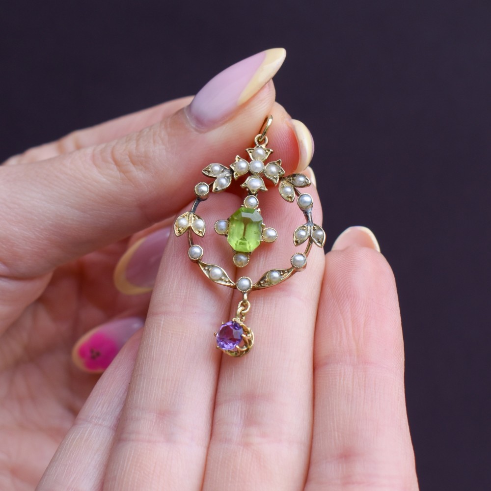 An Edwardian 15ct gold openwork lavalier pendant set with seed pearls, featuring an oval green peridot central stone and a suspended round purple amethyst drop. View VII