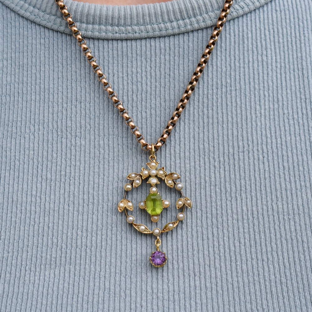 An Edwardian 15ct gold openwork lavalier pendant set with seed pearls, featuring an oval green peridot central stone and a suspended round purple amethyst drop. View VIII