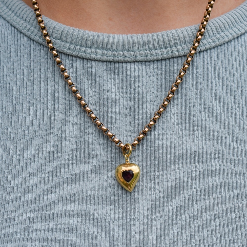 An antique yellow gold puffy heart-shaped charm featuring a central heart-cut purple amethyst paste gem. View IX