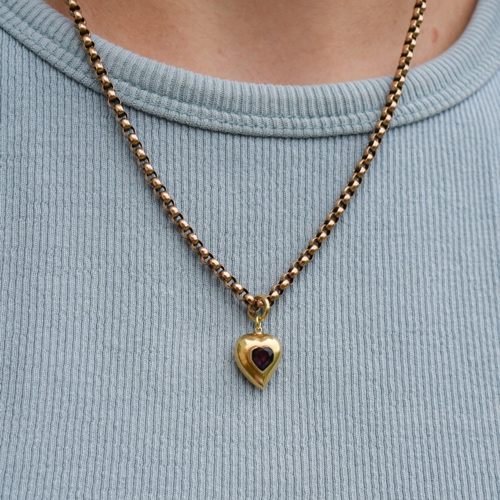 An antique yellow gold puffy heart-shaped charm featuring a central heart-cut purple amethyst paste gem. View X