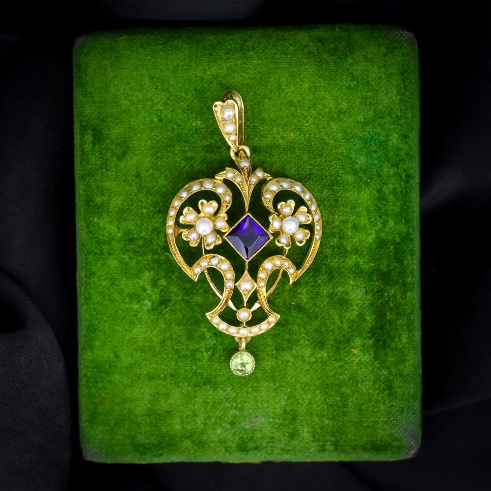 An ornate openwork 15ct gold Edwardian pendant decorated with seed pearls, a square central amethyst, and a hanging round peridot drop.