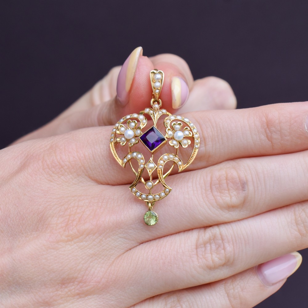 An ornate openwork 15ct gold Edwardian pendant decorated with seed pearls, a square central amethyst, and a hanging round peridot drop. View VI