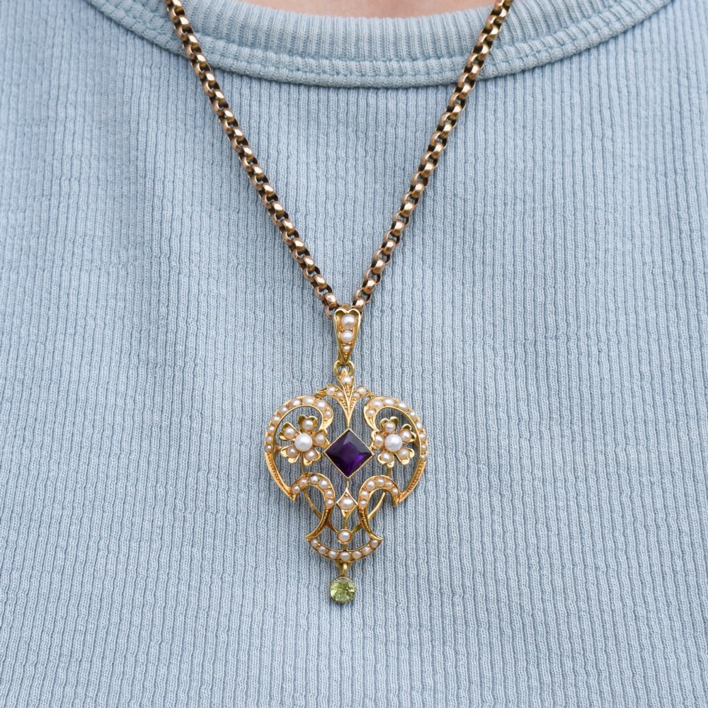 An ornate openwork 15ct gold Edwardian pendant decorated with seed pearls, a square central amethyst, and a hanging round peridot drop. View IX