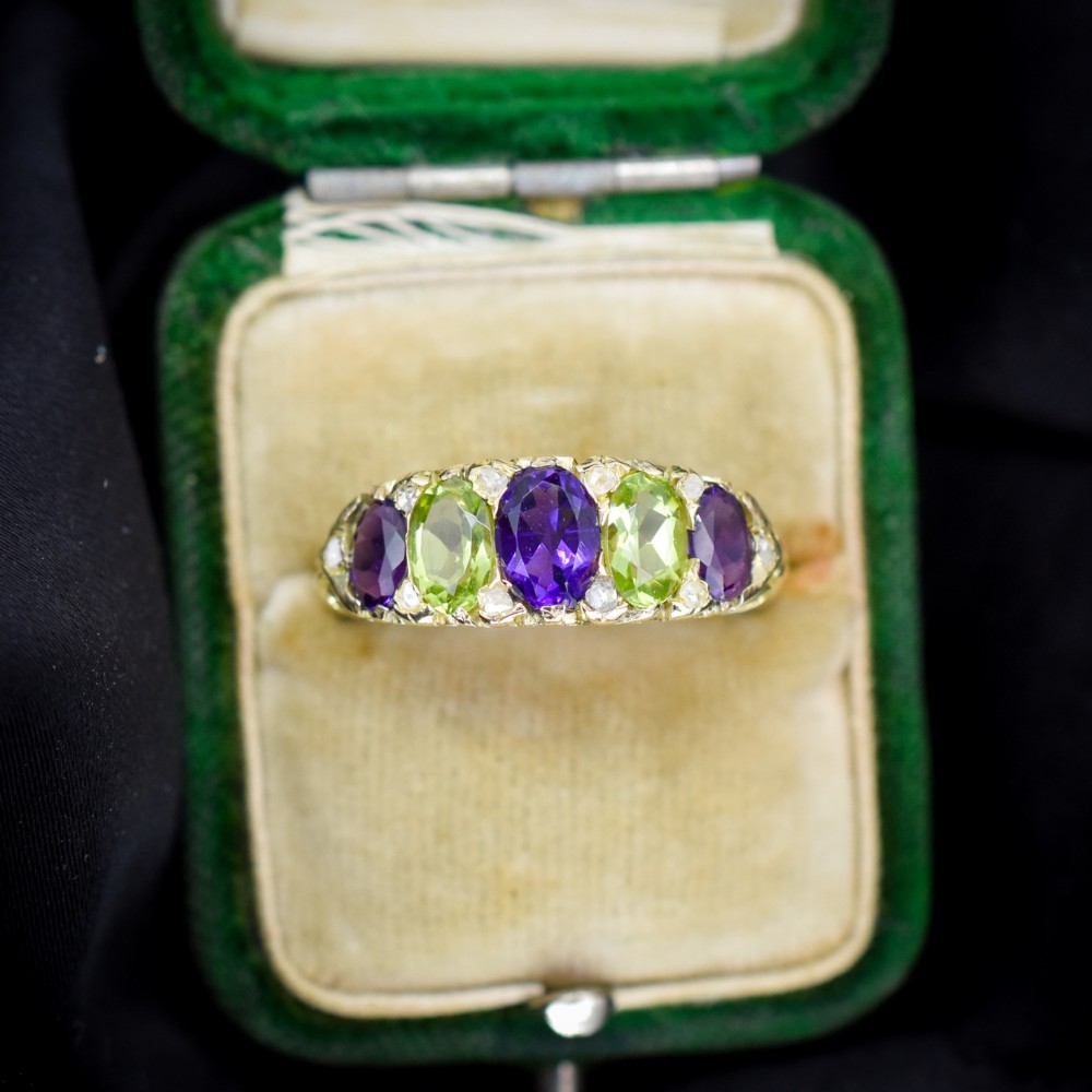 An antique 18ct yellow gold five-stone ring featuring alternating oval amethysts and peridots set with small diamond accents in a carved gallery.