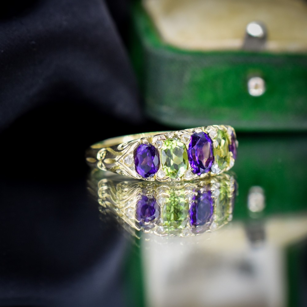 An antique 18ct yellow gold five-stone ring featuring alternating oval amethysts and peridots set with small diamond accents in a carved gallery. View IV