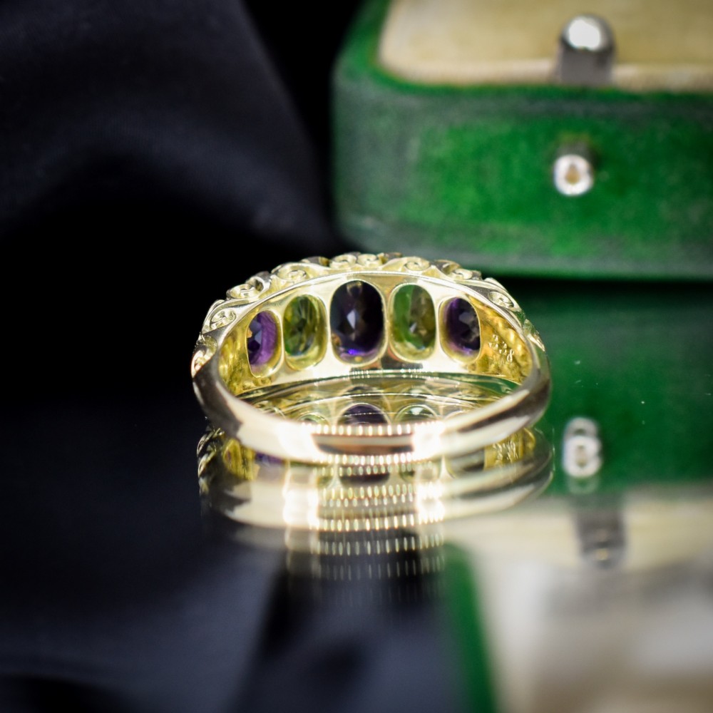 An antique 18ct yellow gold five-stone ring featuring alternating oval amethysts and peridots set with small diamond accents in a carved gallery. View VI