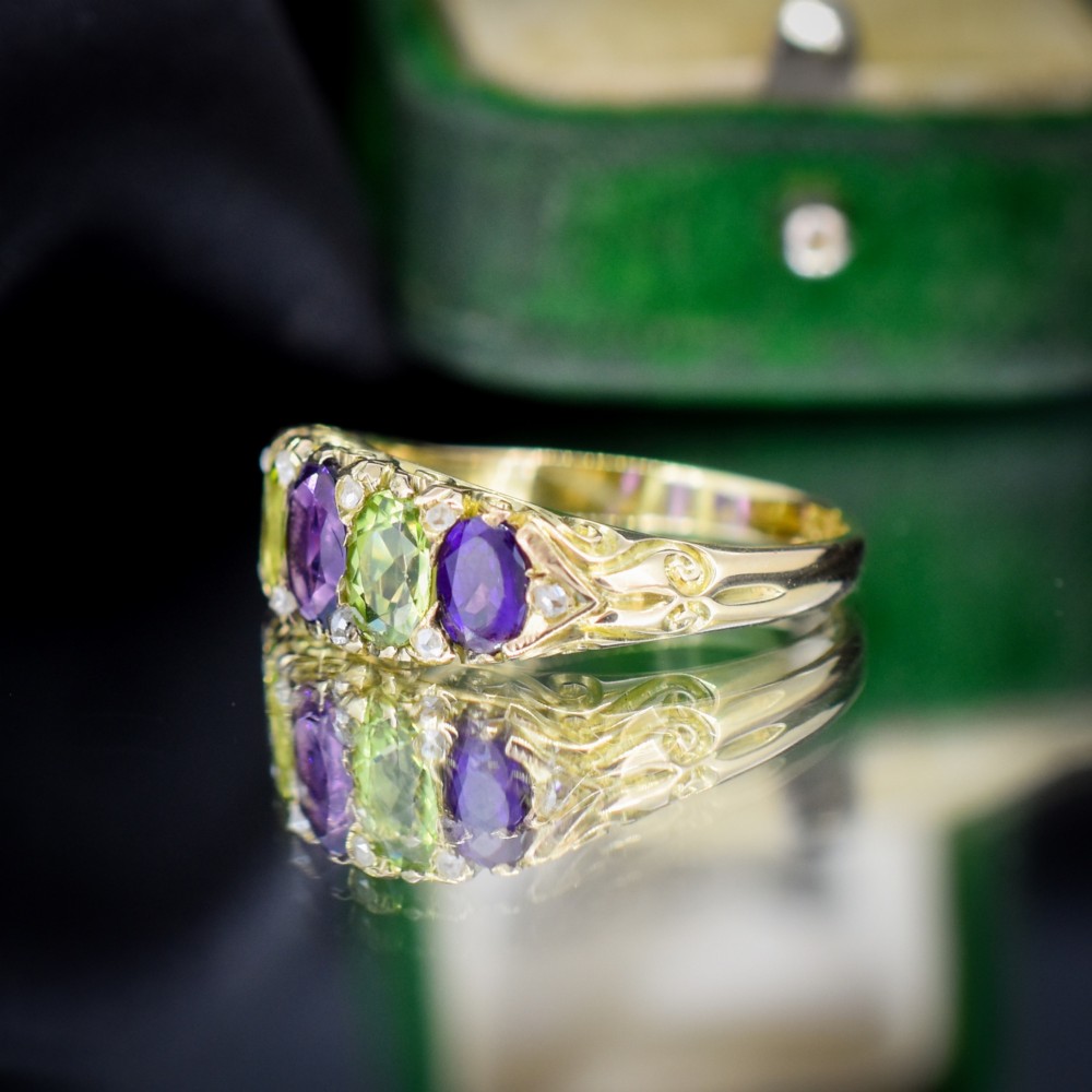 An antique 18ct yellow gold five-stone ring featuring alternating oval amethysts and peridots set with small diamond accents in a carved gallery. View VII