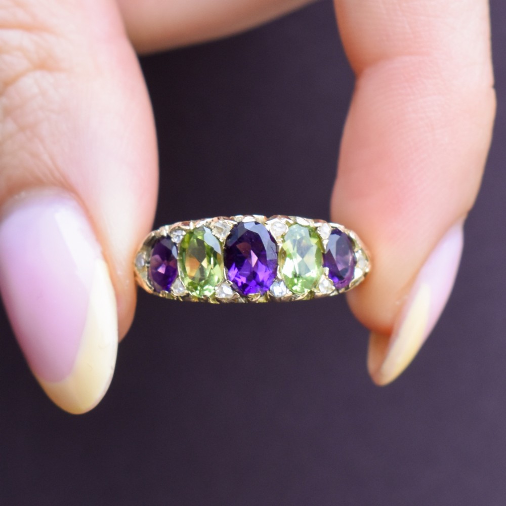 An antique 18ct yellow gold five-stone ring featuring alternating oval amethysts and peridots set with small diamond accents in a carved gallery. View VIII