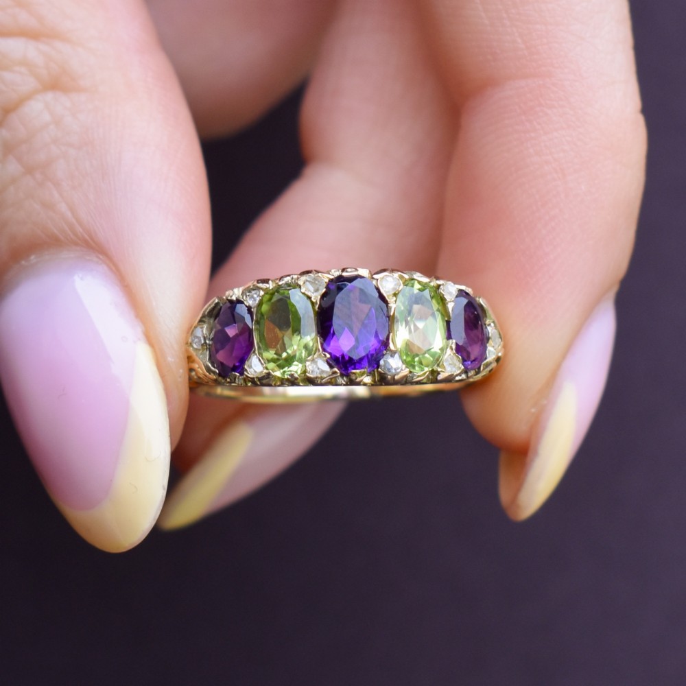An antique 18ct yellow gold five-stone ring featuring alternating oval amethysts and peridots set with small diamond accents in a carved gallery. View IX