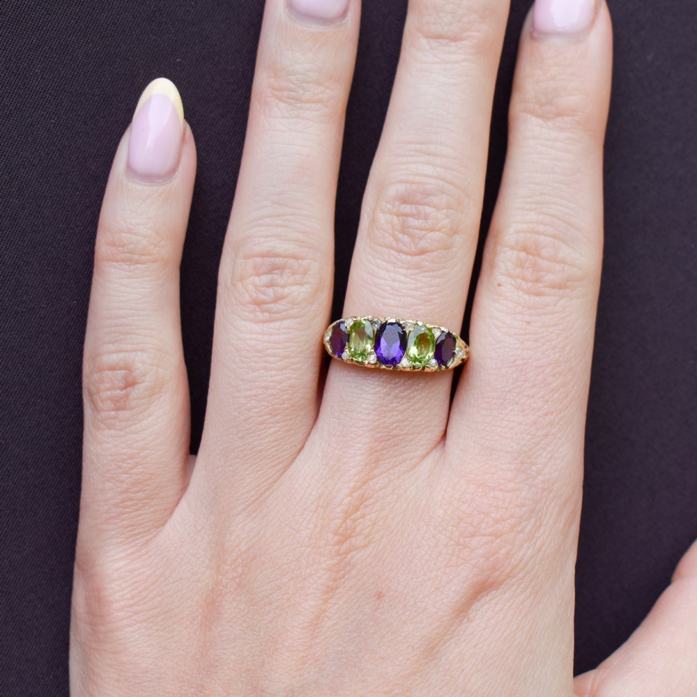 An antique 18ct yellow gold five-stone ring featuring alternating oval amethysts and peridots set with small diamond accents in a carved gallery. View X
