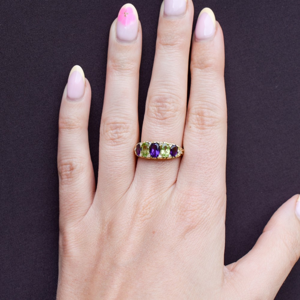 An antique 18ct yellow gold five-stone ring featuring alternating oval amethysts and peridots set with small diamond accents in a carved gallery. View XI