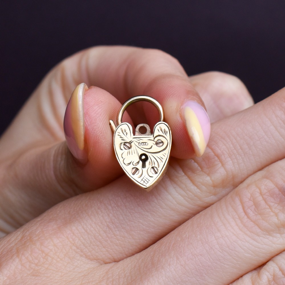 A 9ct yellow gold heart-shaped padlock charm featuring hand-engraved scrollwork and a keyhole detail. View VII