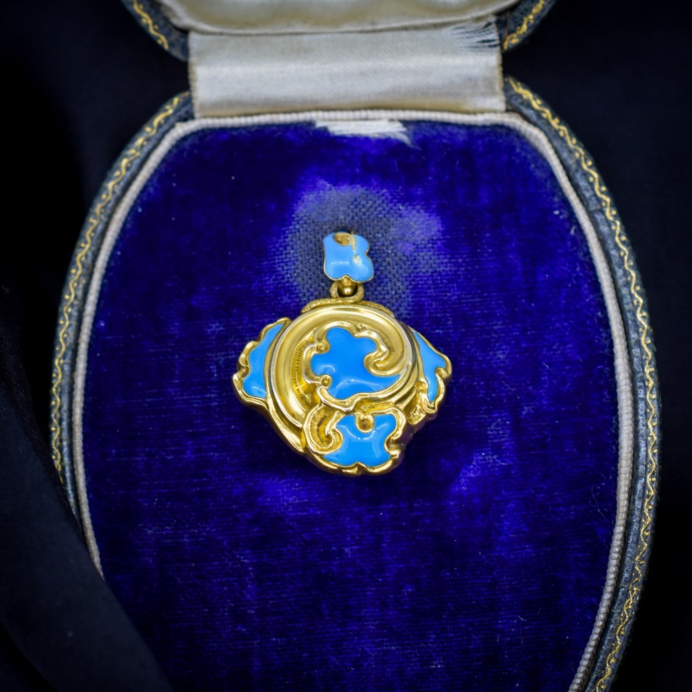 An antique 18ct yellow gold pendant featuring swirling scrollwork inlaid with vibrant turquoise blue enamel.