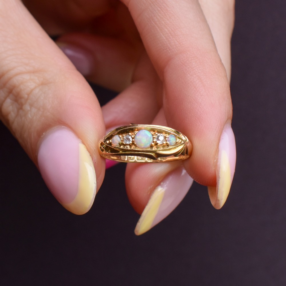 An Edwardian 18ct yellow gold boat ring set with three cabochon natural opals and two small diamonds within a carved scrollwork gallery. View VI