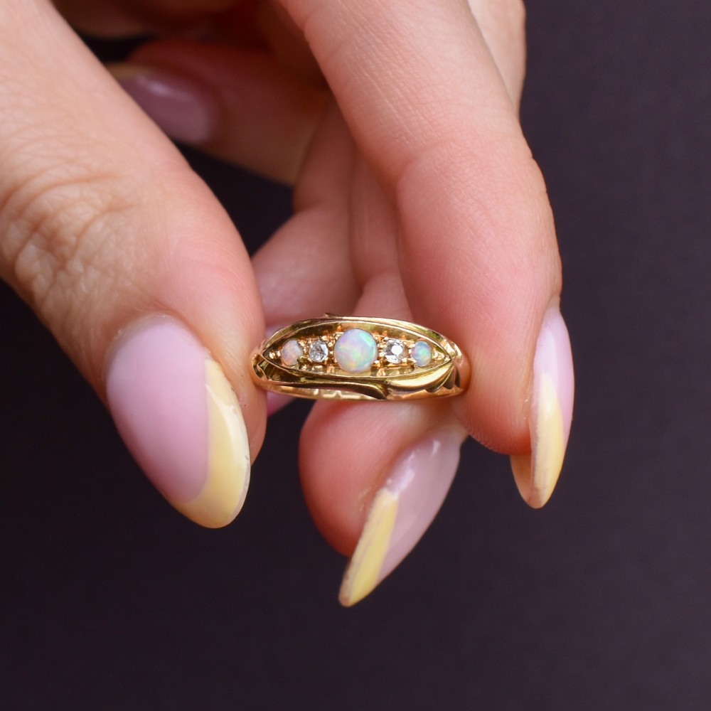 An Edwardian 18ct yellow gold boat ring set with three cabochon natural opals and two small diamonds within a carved scrollwork gallery. View VII