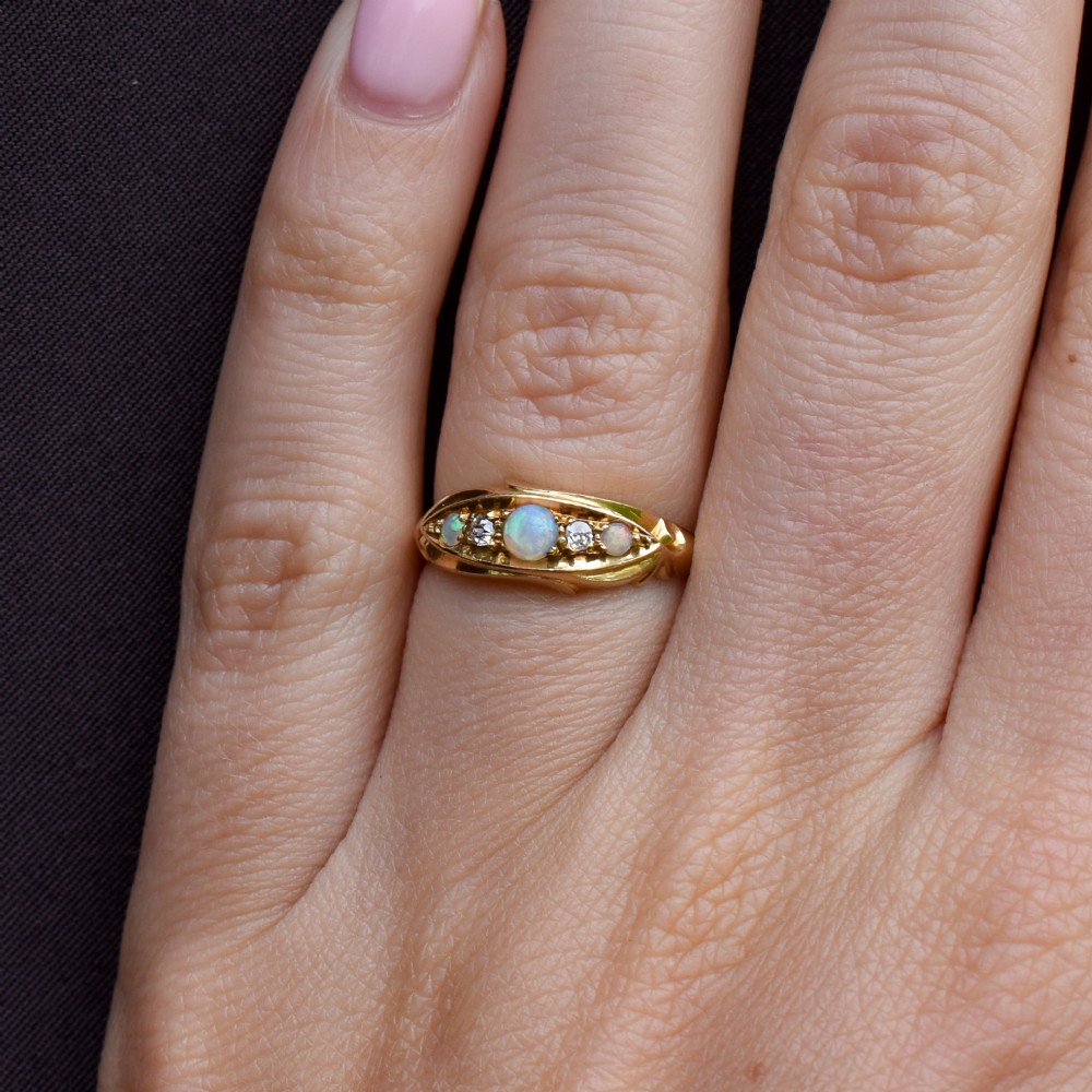 An Edwardian 18ct yellow gold boat ring set with three cabochon natural opals and two small diamonds within a carved scrollwork gallery. View IX