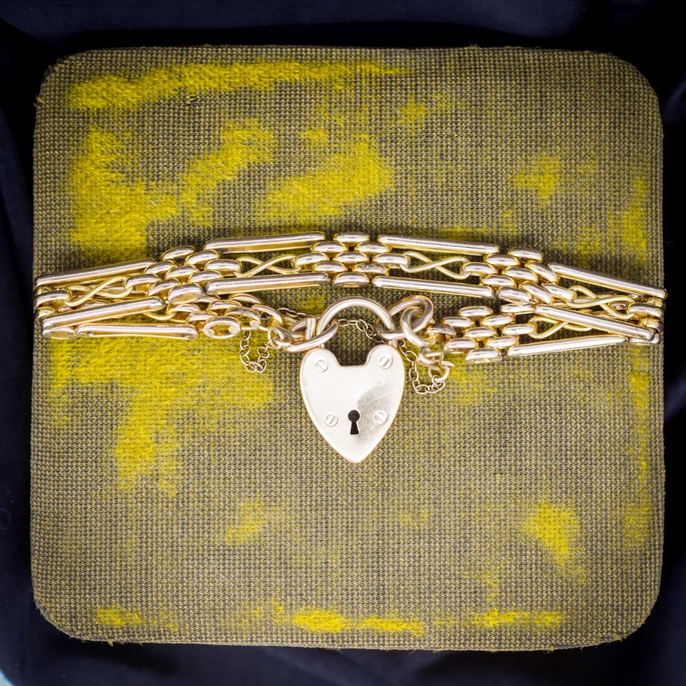 An antique rolled gold gate link bracelet featuring multi-row interlocking bars and a central heart-shaped padlock clasp with a safety chain.