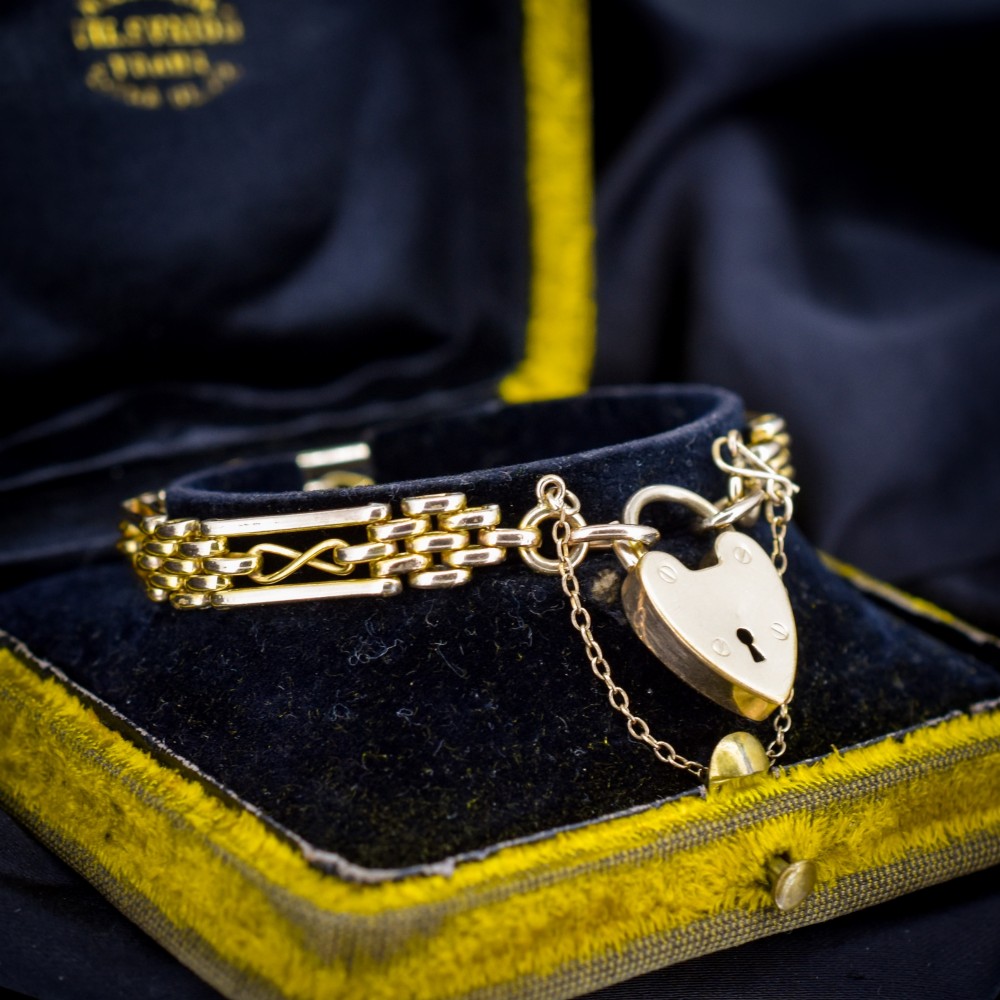 An antique rolled gold gate link bracelet featuring multi-row interlocking bars and a central heart-shaped padlock clasp with a safety chain. View IV