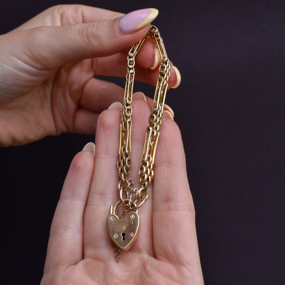 An antique rolled gold gate link bracelet featuring multi-row interlocking bars and a central heart-shaped padlock clasp with a safety chain. View IX