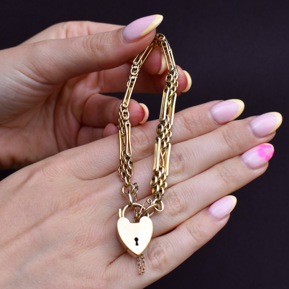 An antique rolled gold gate link bracelet featuring multi-row interlocking bars and a central heart-shaped padlock clasp with a safety chain. View X