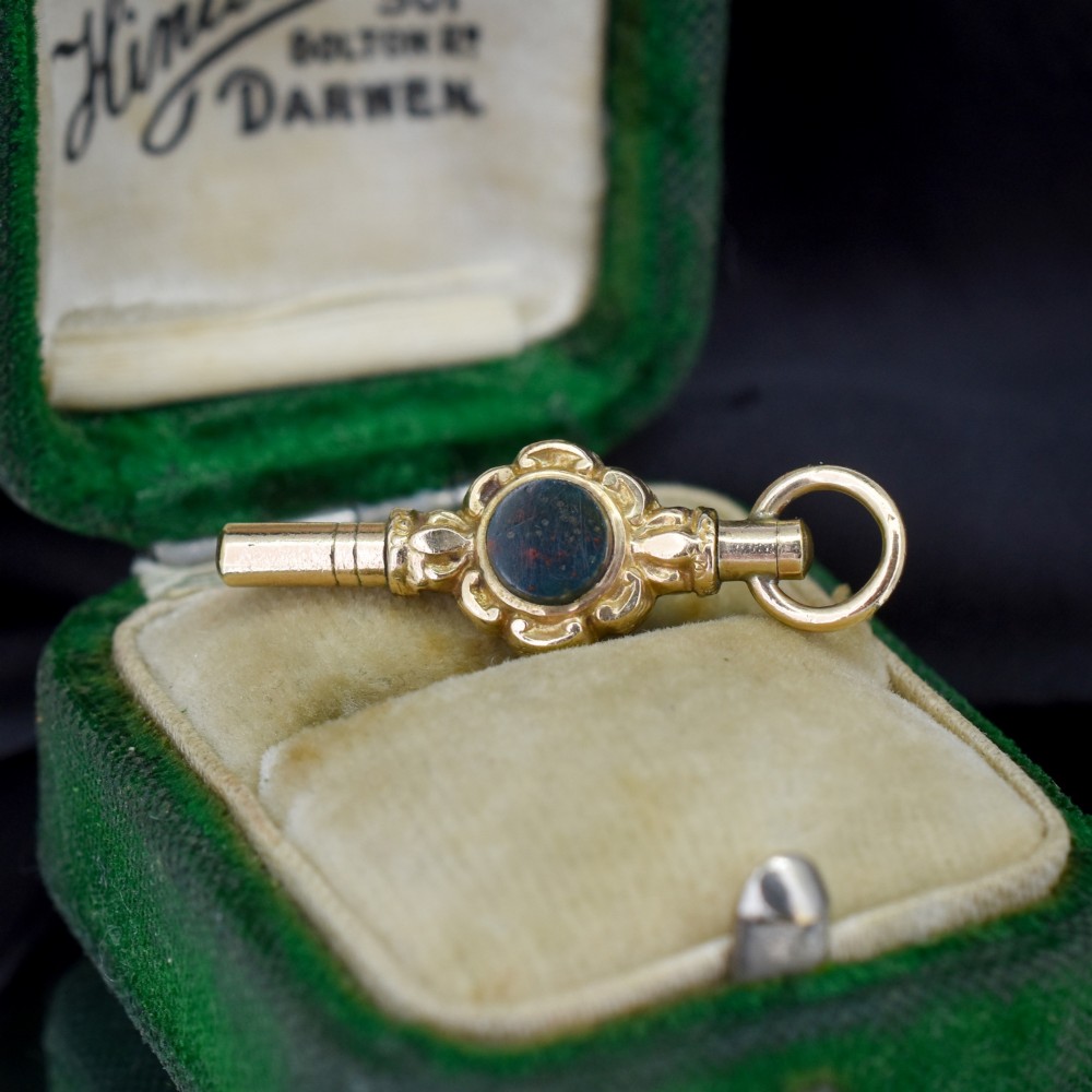 A gold-cased pocket watch key set with a central round dark green agate stone and fitted with a top suspension ring.