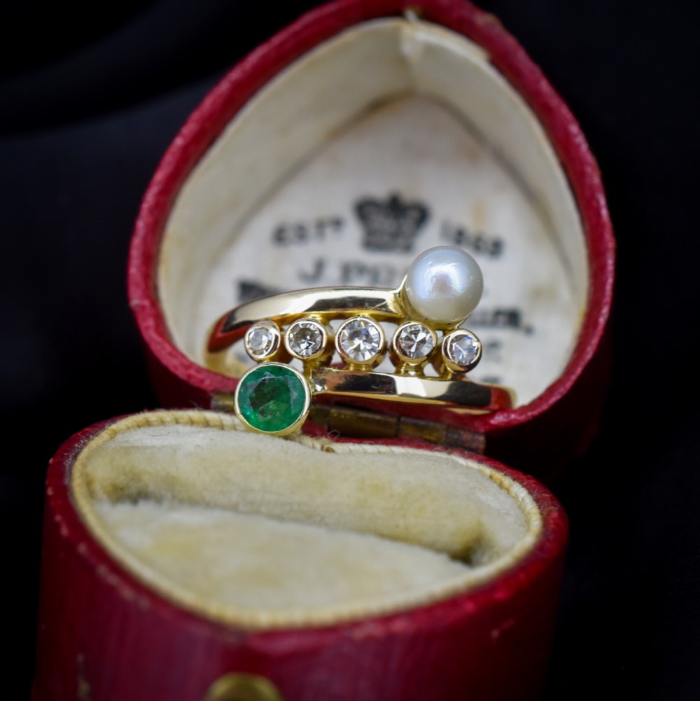 A 14ct yellow gold bypass twist ring set with a single pearl, a round green emerald, and five bezel-set diamonds across the band. View II